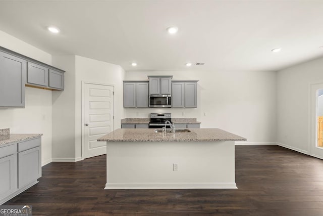 kitchen with a kitchen island with sink, appliances with stainless steel finishes, light stone counters, and dark hardwood / wood-style floors