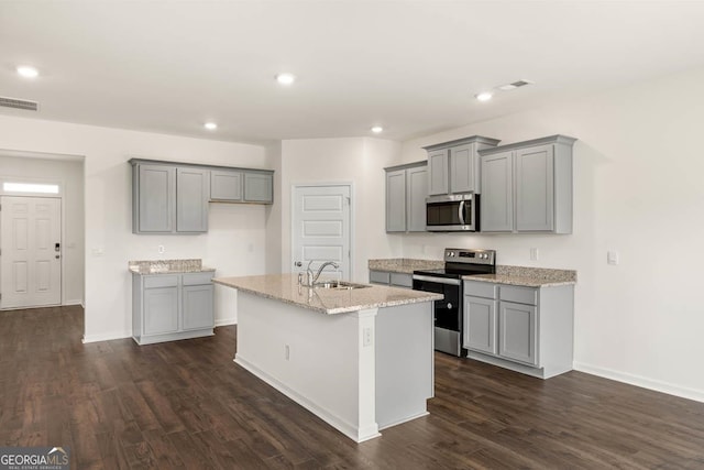 kitchen with dark hardwood / wood-style floors, light stone countertops, gray cabinetry, appliances with stainless steel finishes, and an island with sink