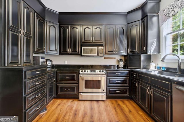 kitchen with crown molding, light wood finished floors, appliances with stainless steel finishes, and a sink