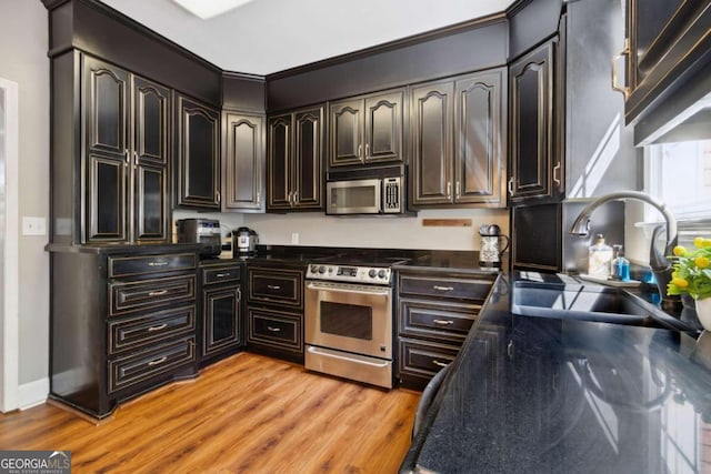 kitchen with light wood-type flooring, a sink, dark countertops, appliances with stainless steel finishes, and baseboards