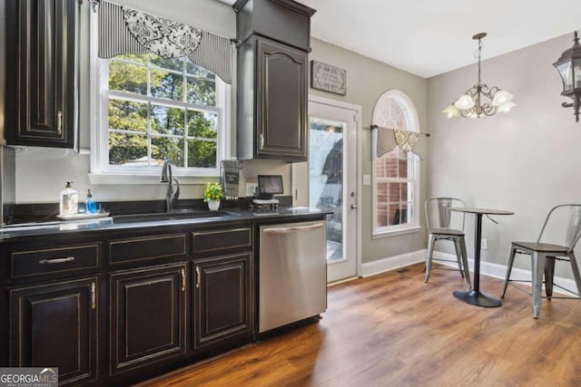 kitchen featuring wood finished floors, baseboards, a sink, dishwasher, and dark countertops