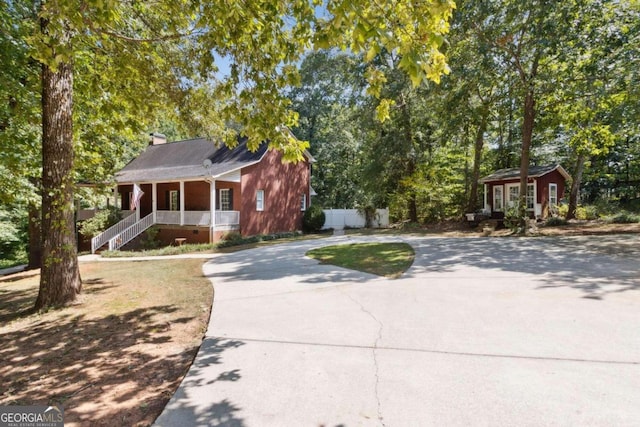 view of front of property featuring curved driveway, a porch, a chimney, and fence