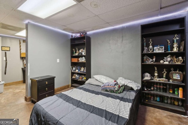 bedroom with baseboards, concrete floors, and a drop ceiling