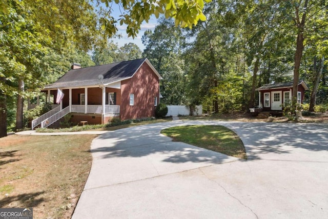 view of front facade with curved driveway, fence, a front yard, covered porch, and a chimney