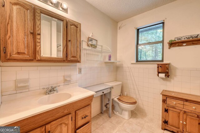 bathroom featuring a wainscoted wall, toilet, vanity, tile patterned floors, and a textured ceiling