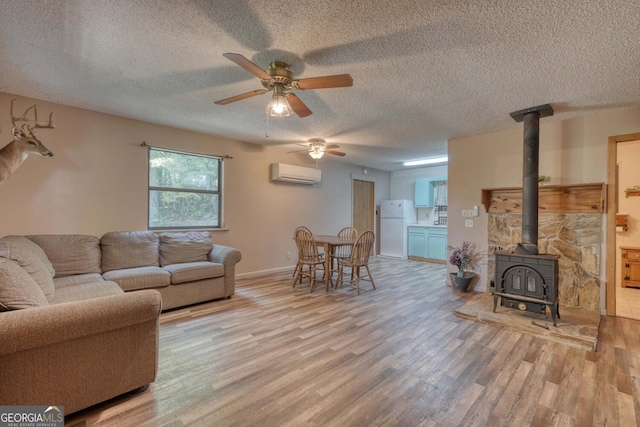 living room with wood finished floors, a wood stove, ceiling fan, a wall mounted air conditioner, and a textured ceiling