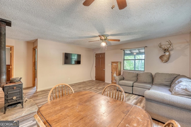 dining room with a wood stove, ceiling fan, light wood-type flooring, and a textured ceiling