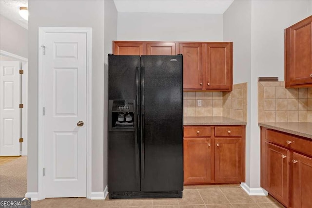 kitchen featuring light tile patterned flooring, light stone countertops, black refrigerator with ice dispenser, and tasteful backsplash