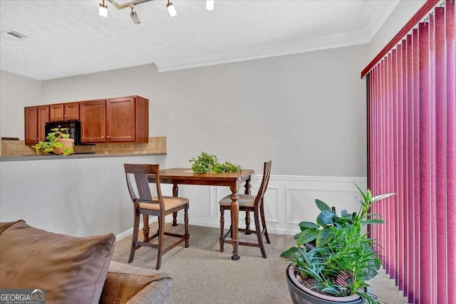 dining space featuring ornamental molding, a textured ceiling, rail lighting, and light colored carpet