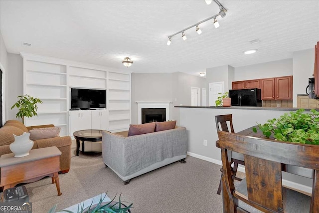 living room with a textured ceiling, rail lighting, light carpet, and built in shelves