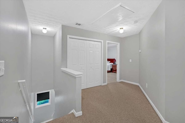 interior space featuring attic access, visible vents, carpet, a textured ceiling, and an upstairs landing