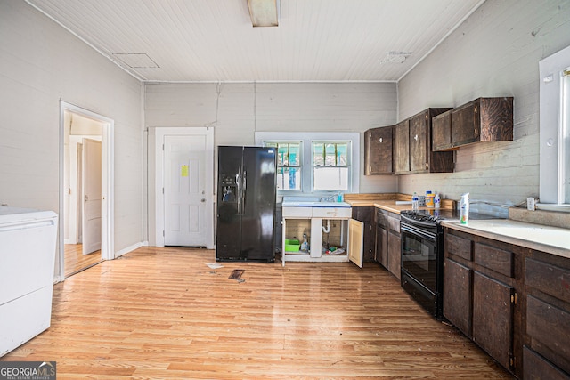 kitchen featuring black appliances, light hardwood / wood-style flooring, wood walls, and dark brown cabinetry