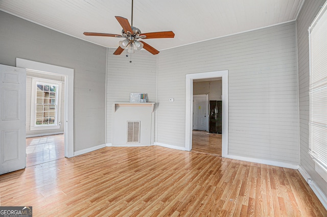 unfurnished living room with ceiling fan, wood walls, wood-type flooring, and a fireplace