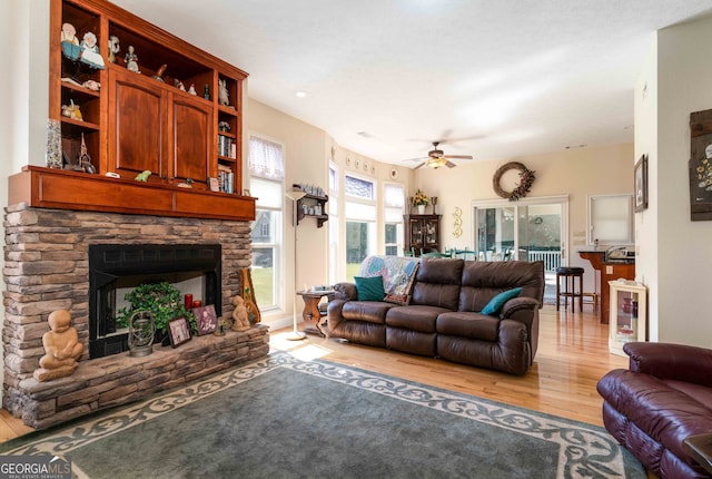 living room with a fireplace, light wood-type flooring, and ceiling fan