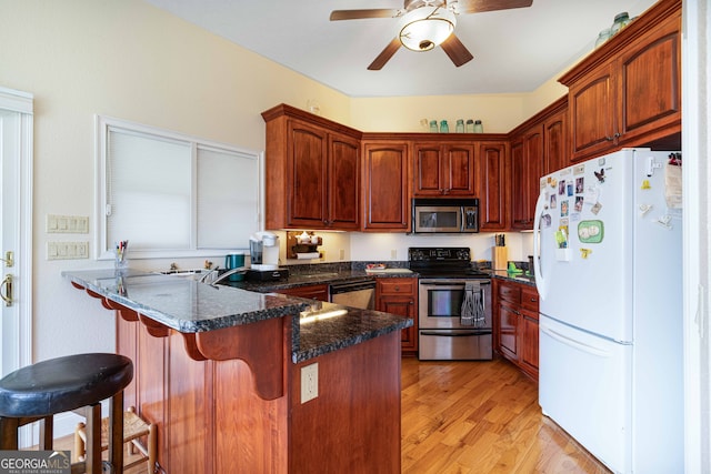 kitchen featuring a kitchen breakfast bar, stainless steel appliances, ceiling fan, dark stone countertops, and light wood-type flooring