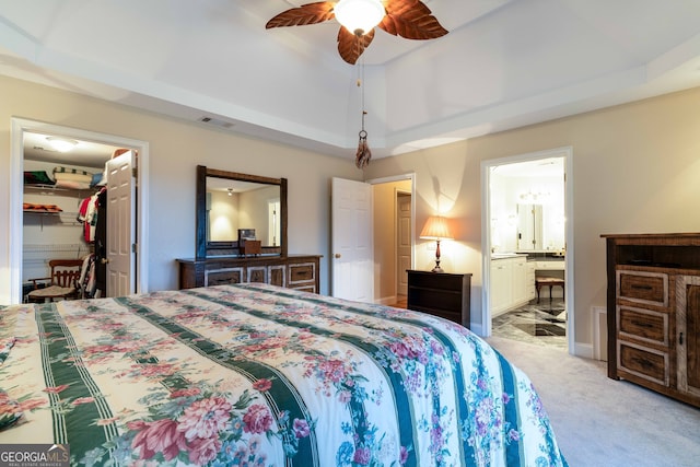 bedroom with a raised ceiling, connected bathroom, ceiling fan, and light colored carpet