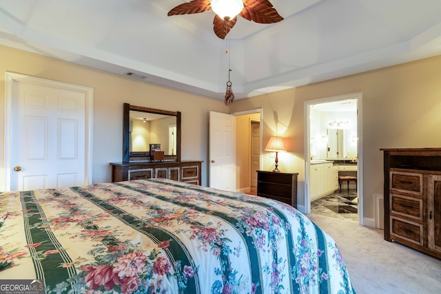 carpeted bedroom featuring a raised ceiling, ensuite bathroom, and ceiling fan