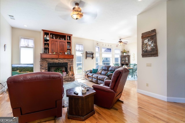 living room featuring ceiling fan, light wood-type flooring, and a fireplace