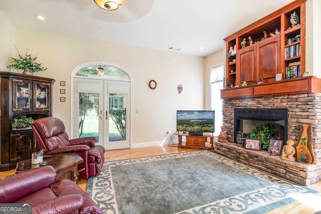 living room with ceiling fan, a stone fireplace, wood-type flooring, and french doors