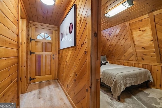 bedroom with vaulted ceiling, wood ceiling, wooden walls, and light hardwood / wood-style flooring