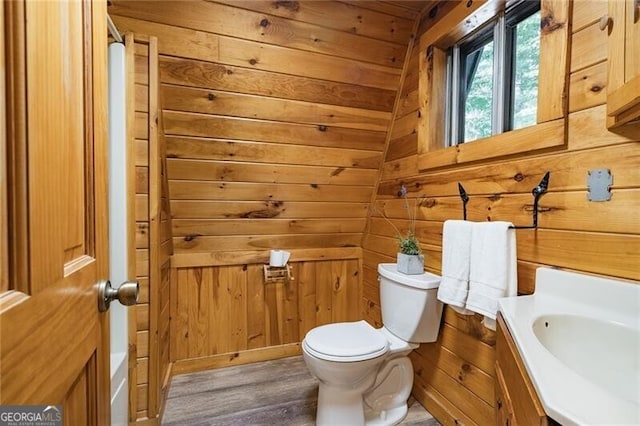 bathroom with hardwood / wood-style flooring, wooden walls, vaulted ceiling, toilet, and vanity