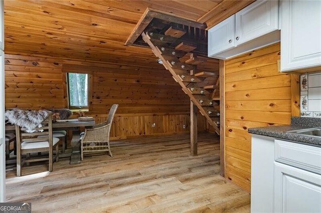 kitchen with wooden ceiling, light hardwood / wood-style flooring, wood walls, and white cabinets