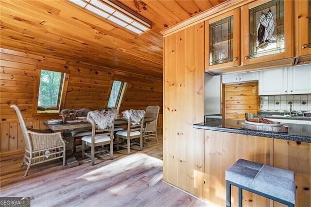 kitchen featuring wood walls, wooden ceiling, decorative backsplash, a skylight, and light wood-type flooring