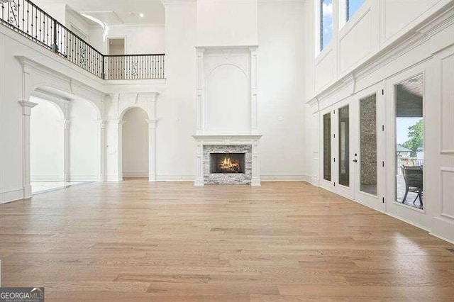 unfurnished living room with crown molding, a high ceiling, french doors, and light hardwood / wood-style floors