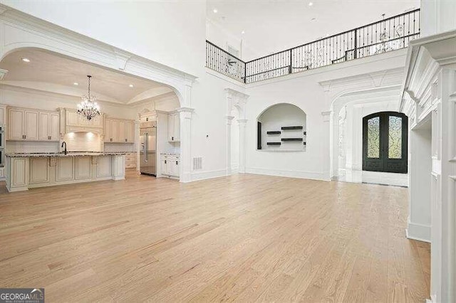 unfurnished living room with a high ceiling, a notable chandelier, light hardwood / wood-style flooring, decorative columns, and sink