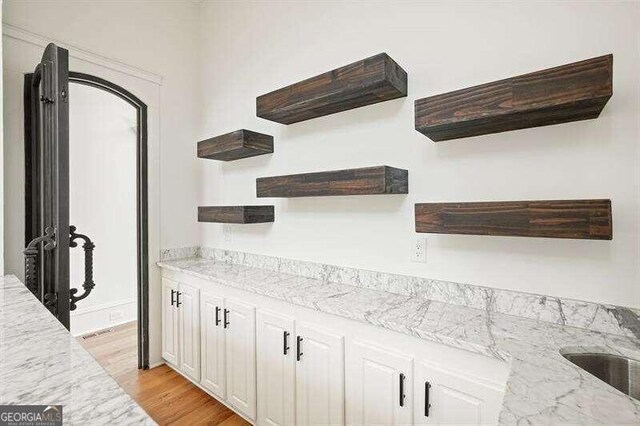 bar with light wood-type flooring, white cabinets, and light stone counters