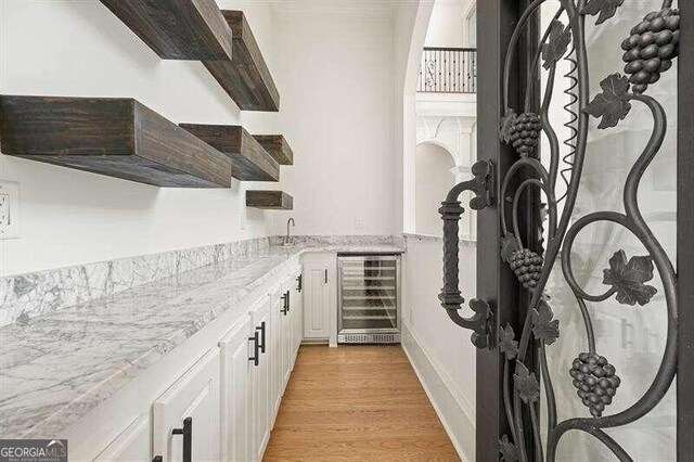 interior space with light hardwood / wood-style flooring, beverage cooler, light stone countertops, and white cabinets