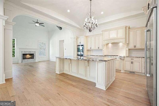 kitchen featuring ceiling fan with notable chandelier, light stone countertops, a premium fireplace, pendant lighting, and a center island with sink