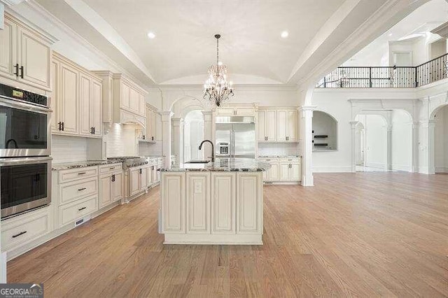 kitchen with decorative columns, light stone counters, cream cabinets, appliances with stainless steel finishes, and light hardwood / wood-style floors