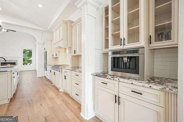 kitchen with sink, decorative backsplash, vaulted ceiling, ornate columns, and light hardwood / wood-style floors