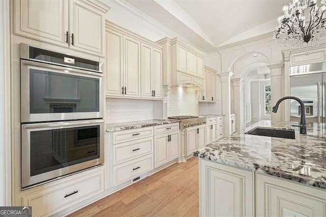 kitchen with vaulted ceiling, light hardwood / wood-style flooring, appliances with stainless steel finishes, decorative columns, and sink