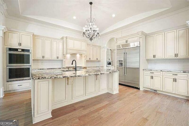 kitchen with a center island with sink, light hardwood / wood-style flooring, stainless steel appliances, and light stone counters