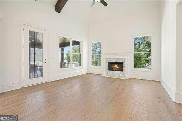 unfurnished living room with a fireplace, beamed ceiling, high vaulted ceiling, light hardwood / wood-style flooring, and ceiling fan