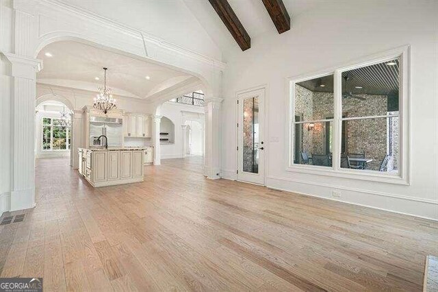 unfurnished living room with light hardwood / wood-style flooring, decorative columns, sink, a chandelier, and vaulted ceiling with beams