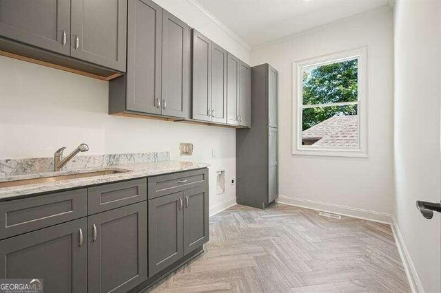 kitchen featuring crown molding, light stone counters, sink, and light parquet flooring