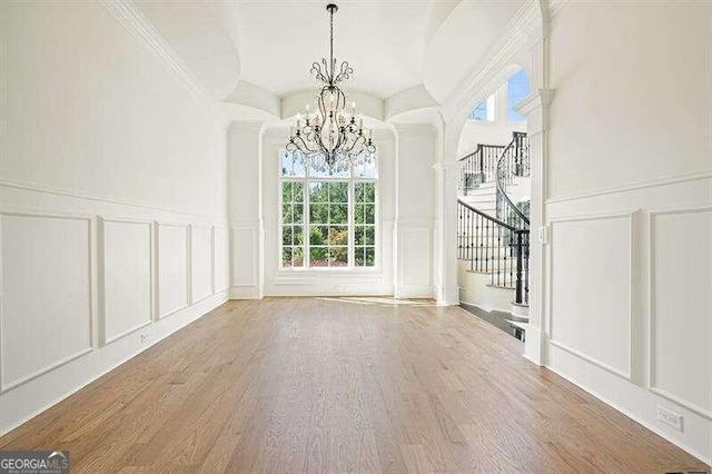 unfurnished dining area with wood-type flooring, a chandelier, and ornamental molding