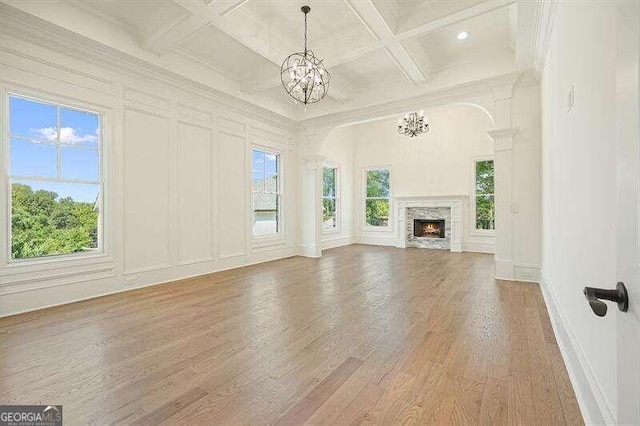 unfurnished living room featuring coffered ceiling, crown molding, an inviting chandelier, beam ceiling, and light hardwood / wood-style floors