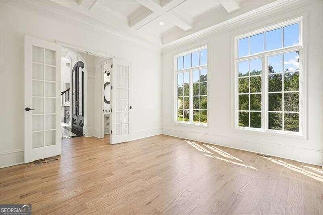 empty room featuring coffered ceiling, wood-type flooring, beam ceiling, and french doors