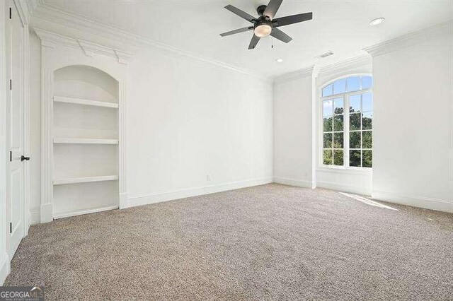 spare room with built in features, ceiling fan, ornamental molding, and carpet floors