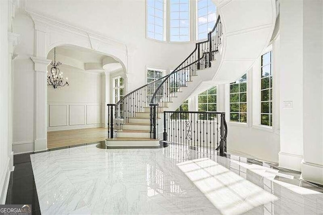 staircase with a towering ceiling, a chandelier, and wood-type flooring