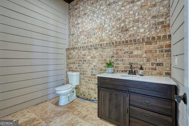 bathroom with toilet, brick wall, and vanity