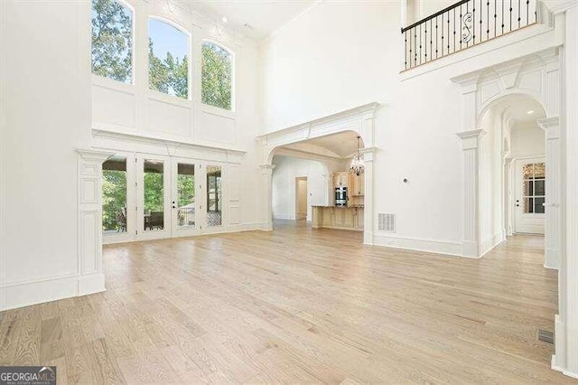 unfurnished living room with light hardwood / wood-style flooring, a towering ceiling, and ornate columns