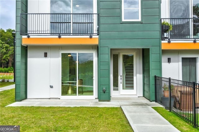 property entrance with fence, a balcony, and a lawn