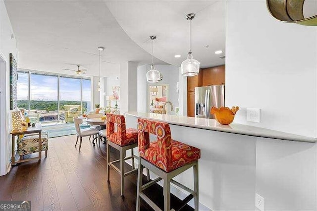 kitchen with decorative light fixtures, dark hardwood / wood-style flooring, kitchen peninsula, a kitchen breakfast bar, and stainless steel fridge with ice dispenser