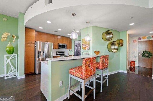 kitchen featuring a kitchen bar, dark wood-type flooring, kitchen peninsula, and stainless steel appliances