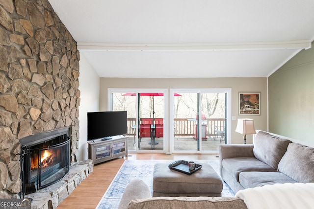 living room featuring a stone fireplace, wood-type flooring, lofted ceiling with beams, and a healthy amount of sunlight